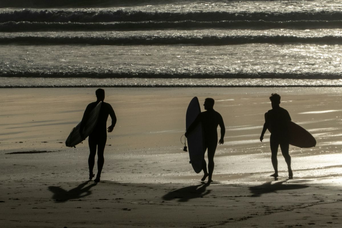Three surfers carrying boards walking on a beach in Cornwall.