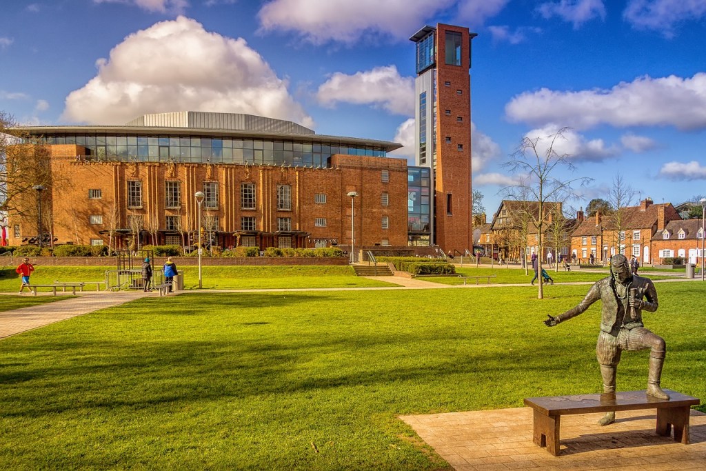 A park with a large brick built building behind in Stratford upon Avon