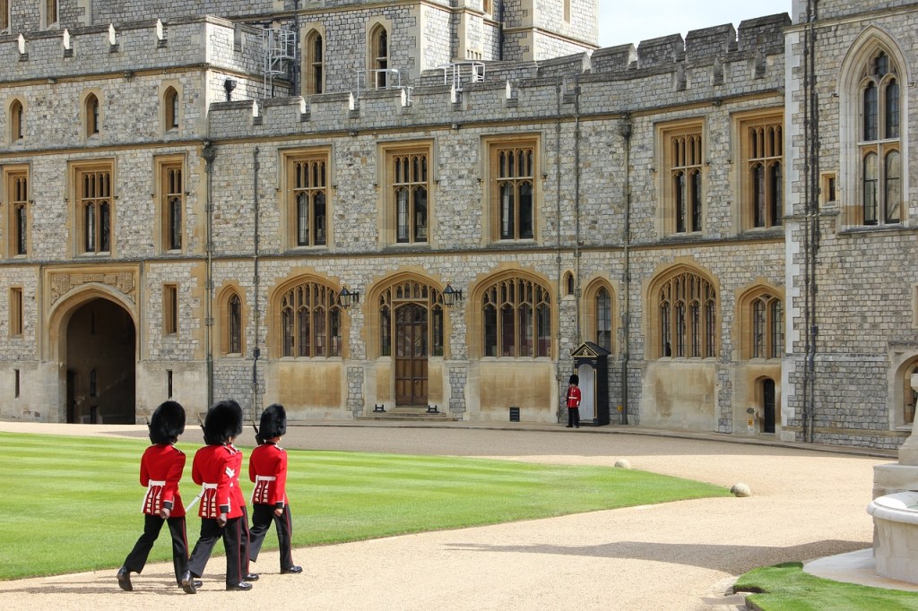 Three guards in red uniforms march in front of Windsor Castle.