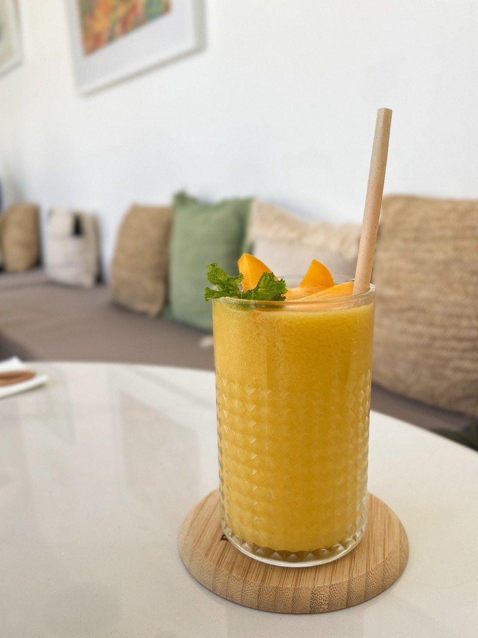 A glass filled with a mango smoothie with a straw in it.