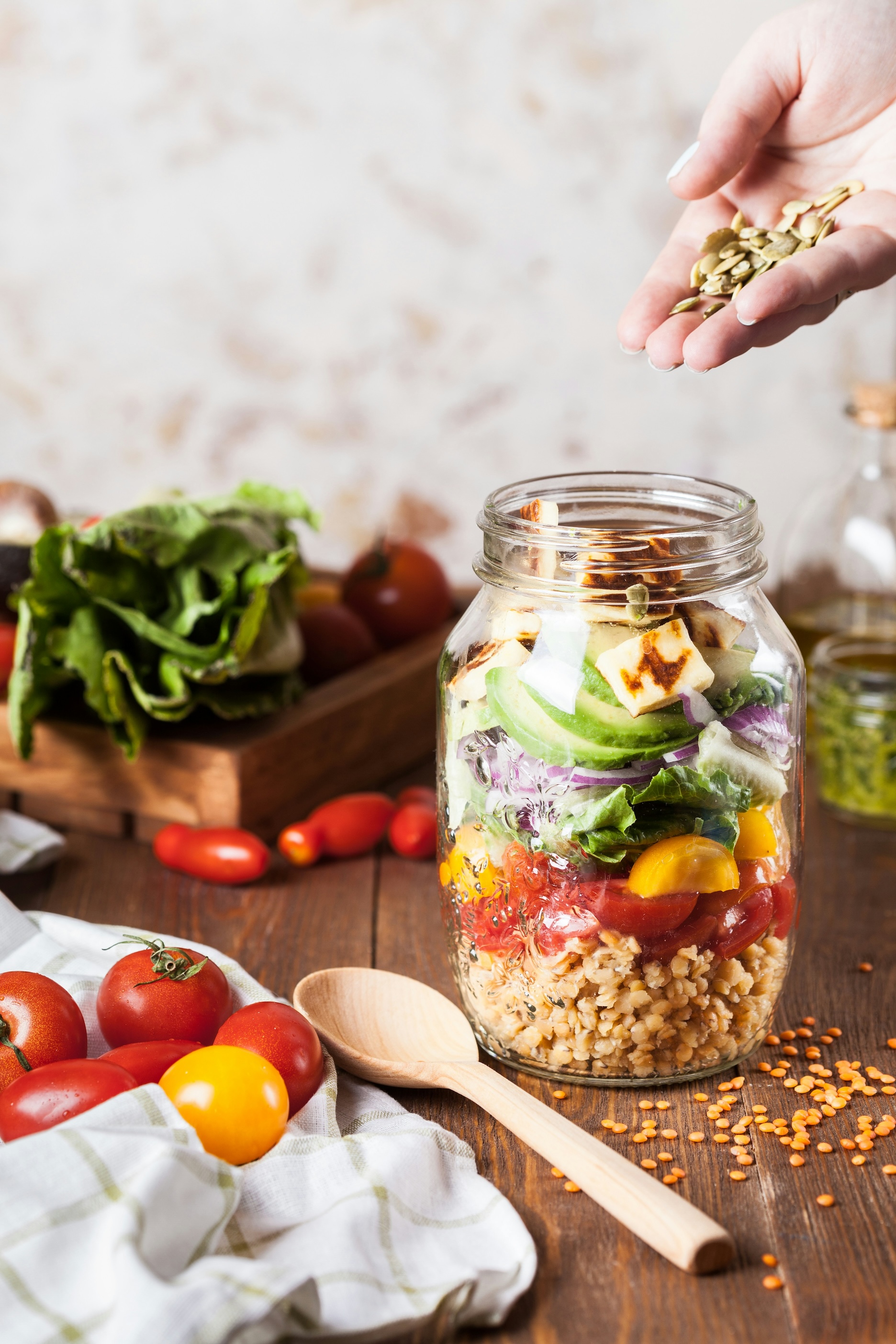 A hand dropping seeds into a jar of salad layers.