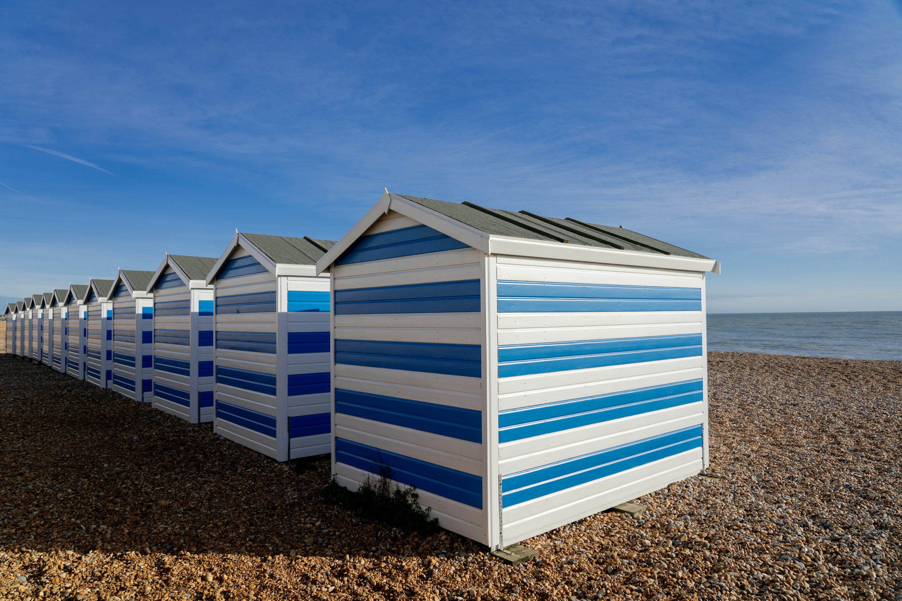 A row of striped beach huts with the sea beyond them.