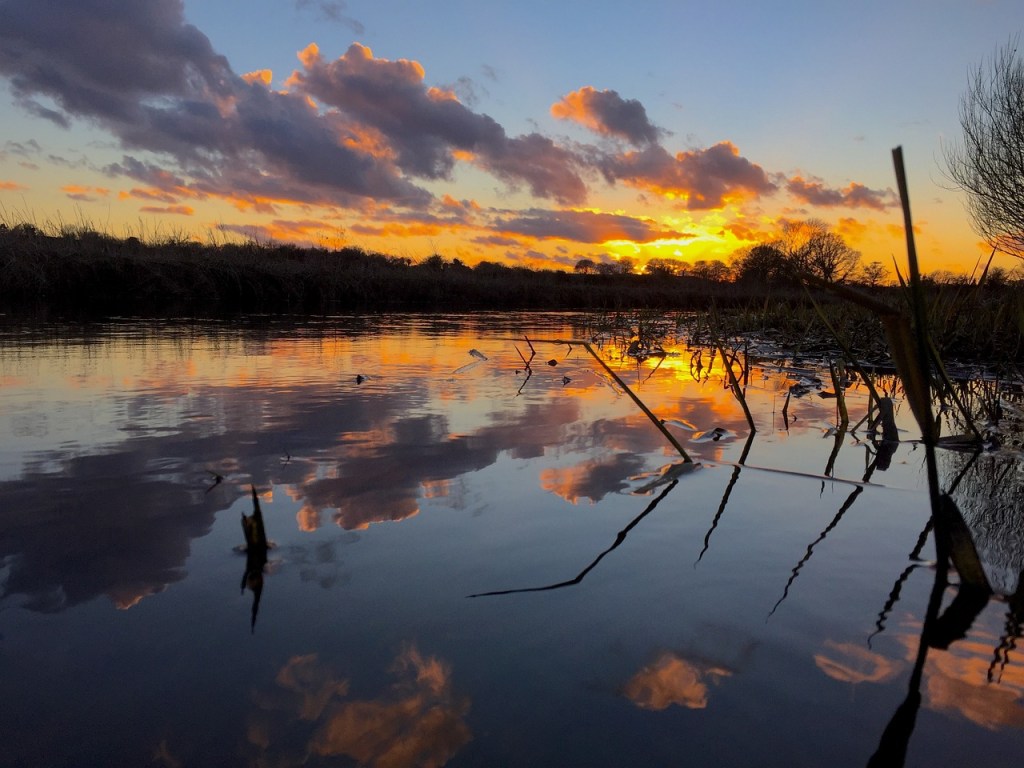 The sun setting over the Norfolk Broads, a wide stretch of water.