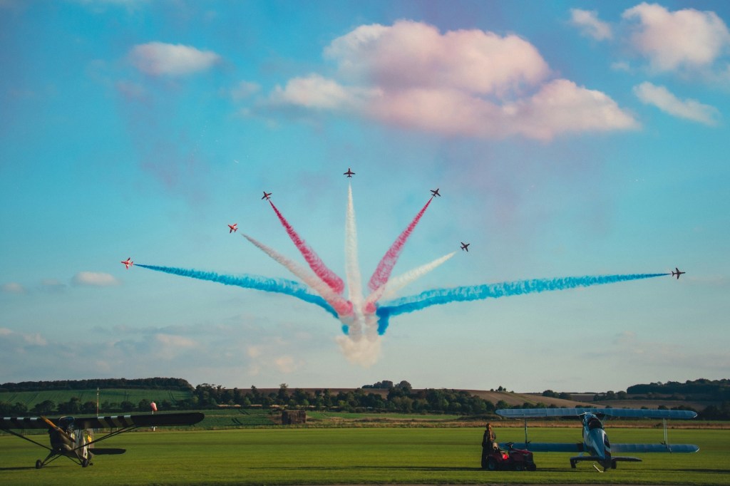 The Red Arrows doing a show with red, white and blue smoke coming from the back of the aircraft.
