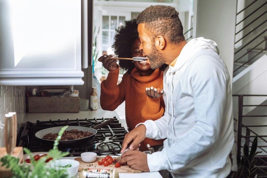 A couple cooking together and smiling.