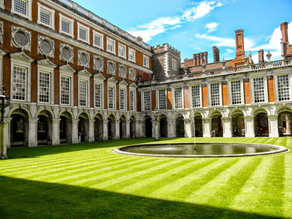 A view of the courtyard of Hampton Court Palace with decorative arches and a lot of windows.