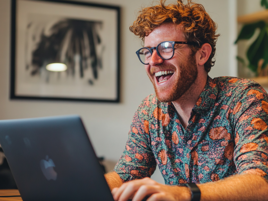 A young man sat at his laptop laughing.
