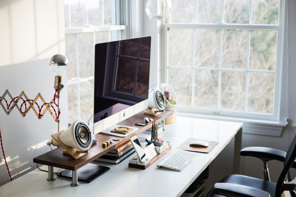A desk setup near a large window with a fun extendable lamp.