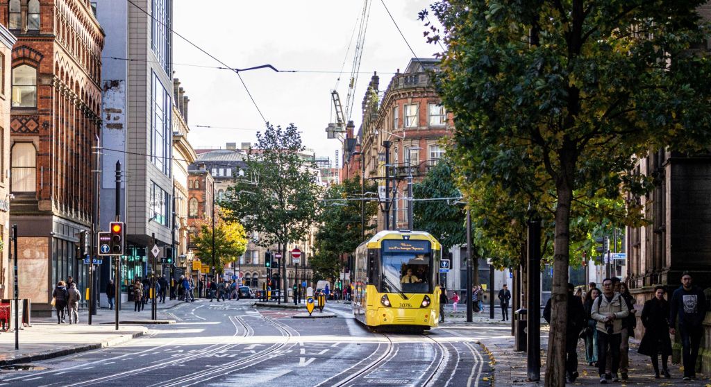 A city street scene in Manchester, UK , with a yellow tram running down the middle of the street.