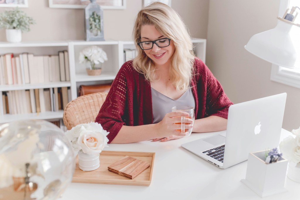 Woman sitting at a desk with laptop smiling and holding a cup of tea.