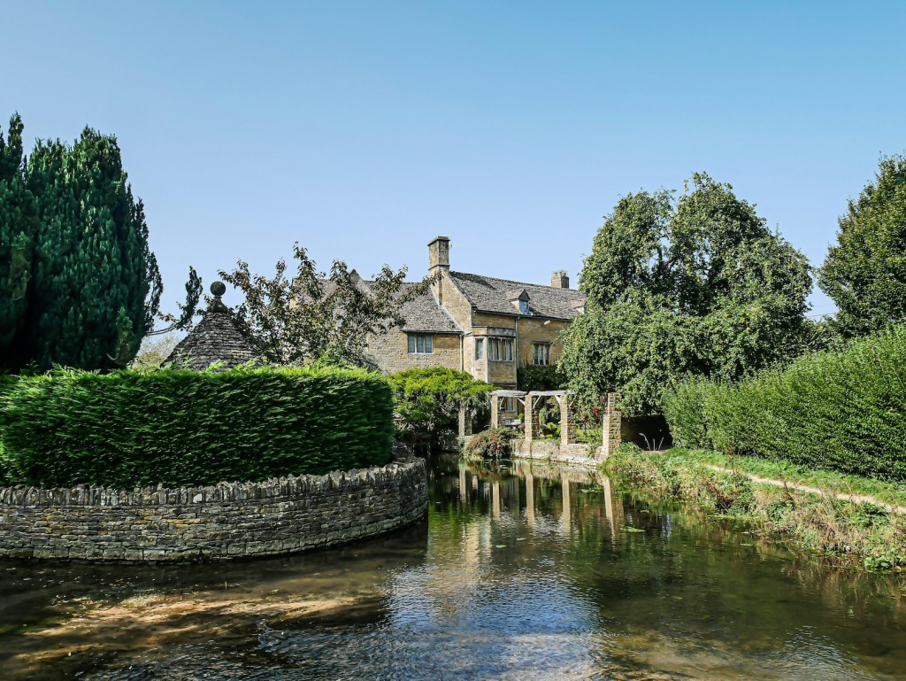 An historic building in the Cotswolds with a stretch of water in the foreground.