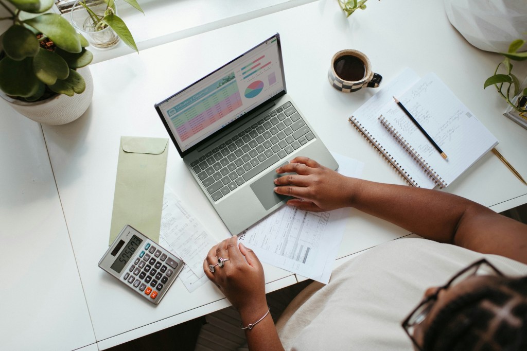 A woman using a laptop and calculator to manage her money.