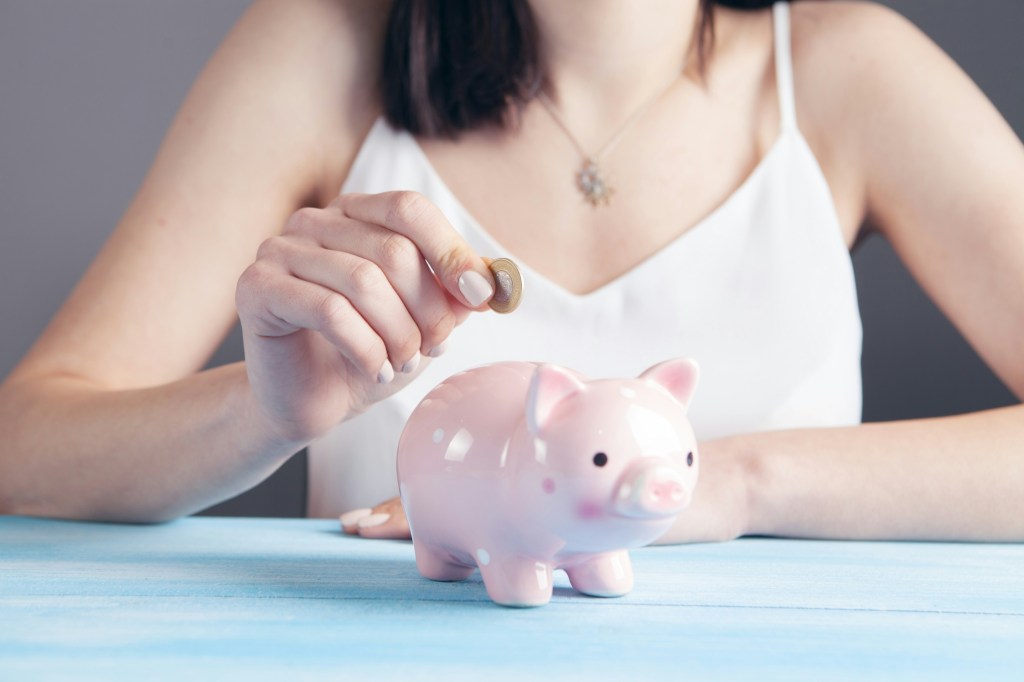 A woman dropping a coin into a piggy bank.
