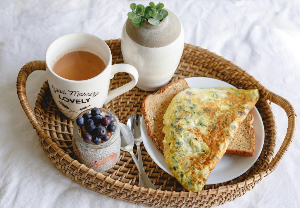 A wooden tray with breakfast laid out on it including a cup of tea, an omelette and some berries.