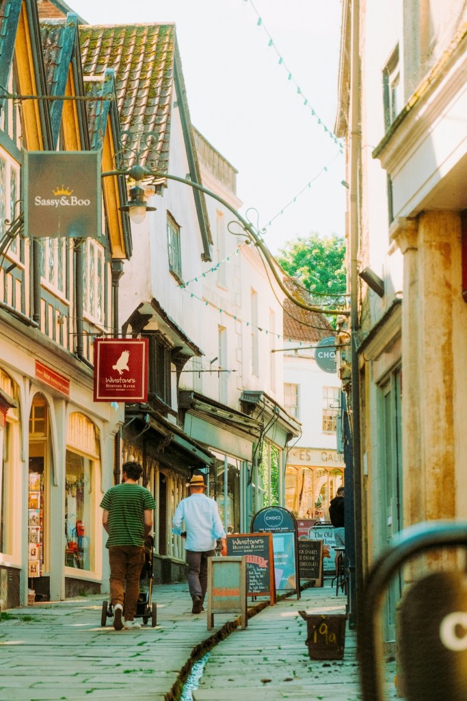 Two men walking up a steep, narrow lane in Frome with pleasant shops.