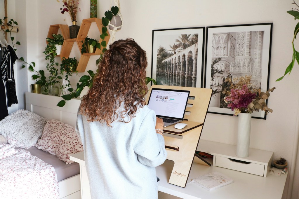 A woman works at a standing desk in a workspace setup in a bedroom.